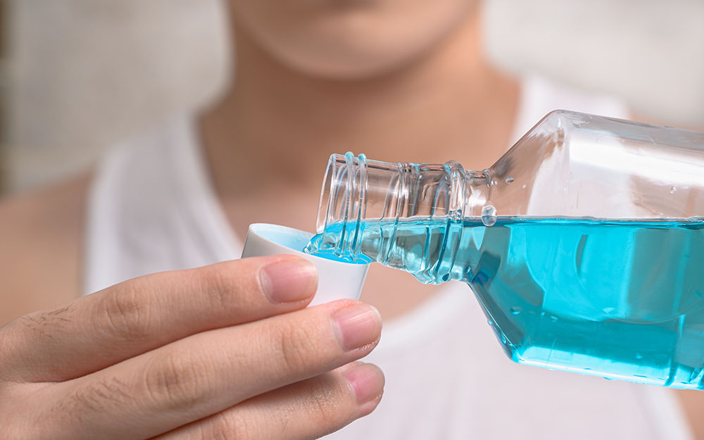 Hand Of Man Pouring Bottle Of Mouthwash Into Cap.